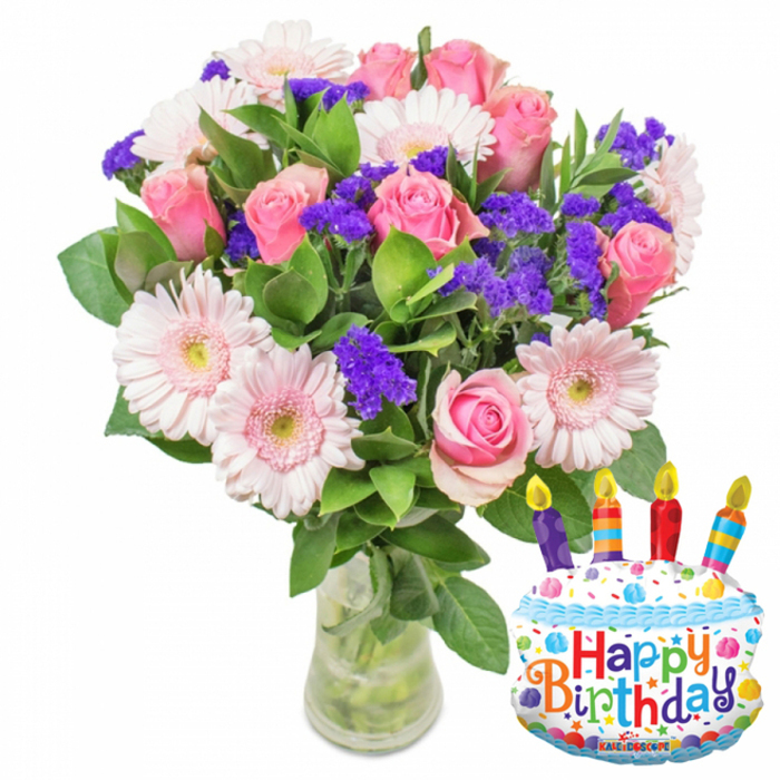 A festive floral gift designed to announce celebration at first glance: a full bouquet of soft-pink roses and pale-pink Gerbera daisies enriched by vivid purple filler flowers and gleaming green foliage, all displayed in a clear glass vase with visible stems and water. The roses are the focal point, their layered, velvety petals opening from a delicate blush to slightly deeper pinks that speak of tenderness and warmth, while the Gerbera daisies, with their broad, flat petals and pale yellow-green centres, introduce a lighter, sunnier note. Scattered throughout are clusters of purple statice or limonium-small, papery florets that add contrast, texture and a festive, almost confetti-like accent against the softer petals. The glossy leaves vary in shape and size, framing the arrangement and lending a lush, garden-fresh backdrop. Beside the bouquet, a metallic cake-shaped balloon brings a playful, modern element: white 'frosting,' blue piped icing, colorful sprinkles, and four striped candles with tiny yellow flames sit atop the design, and the phrase Happy Birthday is printed across the cake in bright multi-coloured letters; the balloon's lower edge bears the small KALEIDOSCOPE brand. As a local florist piece, this arrangement is exactly the sort of thoughtful birthday surprise customers request in Golders Green-easy to carry from our shop on Golders Green Road or to deliver around Hoop Lane and Finchley Road-combining traditional blooms, tactile fillers and a celebratory accessory that together create warmth, visual cheer, and the quiet scent of fresh-cut roses.