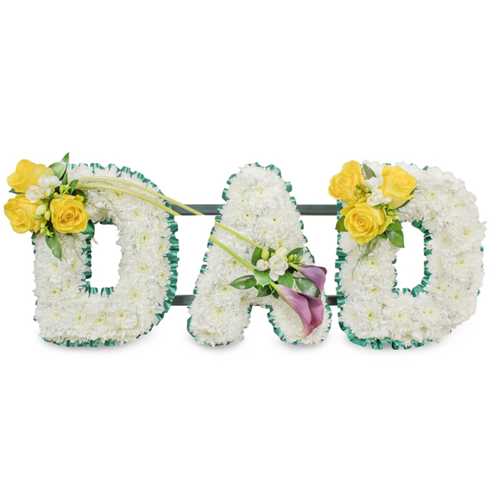 A striking, dignified tribute crafted to read from a distance, the word DAD stands in large, voluminous letters made entirely from pristine white spray chrysanthemums, their small heads packed tightly to form soft, rounded surfaces. Each letter is given a tailored boundary with a ruffled dark green satin ribbon that creates a bold contrast and a refined frame; the ribbon's texture catches the light differently than the blooms, adding subtle depth. Behind the letters, narrow dark green metal support bars run horizontally, visible in the negative space and reassuringly suggesting solidity and cohesion. The arrangement sits against a clean white background so every petal and ribbon fold is clearly legible.  Accents are placed to speak in colour and feeling. On the left D a radiant grouping of sunny yellow roses-three to four full blooms-sits on the upper left curve with delicate white filler flowers like freesias or gypsophila and fresh green leaves; two elegant, bare green stems extend diagonally toward the centre, introducing movement. The centre A is adorned low on its left leg by two deep purple or burgundy calla lilies; their slender, trumpet-shaped forms lend a refined stillness, surrounded by tiny white accents and glossy foliage. The right D mirrors the left, providing visual symmetry and comfort. The scent is quietly floral-clean freesia and soft rose-evoking bright afternoons and remembered laughter. Appropriate for memorials at local sites from Golders Green crematorium to small family gatherings in Hampstead Garden Suburb, this bespoke piece balances tranquil white, warm yellow, and reverent purple in an elegant farewell to a father.