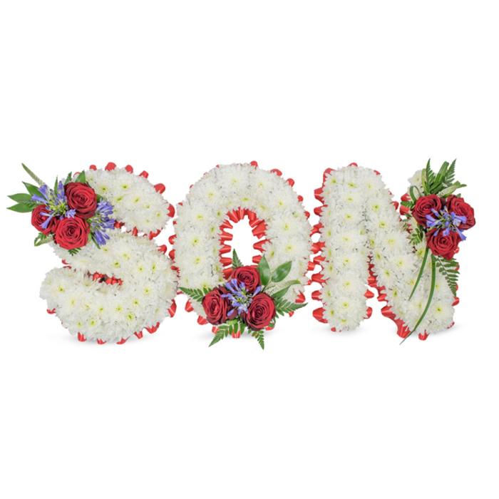 A poignant and carefully constructed memorial arrangement presents the word SON in large, three-dimensional capitals on a clear white background that emphasises the piece's purity and form. Each letter is densely covered with small, pristine white chrysanthemums whose soft, pillowy heads are arranged with exacting attention to create a uniform, cloud-like texture. Around the outer edge of each letter a bright red satin ribbon is folded into a scalloped trim, the pleats catching subtle studio light and neatly defining every curve and corner. The composition is enlivened by three distinctive accent clusters: the S bears a grouping at its top-left curve, the O carries one settled into its bottom centre, and the N is graced with a spray on its top-right vertical. These accents are built from velvety deep-red roses, upright stems of blue-purple Liatris or similar spiked blooms, and generous dark green foliage including delicate fern fronds and trailing leaves that soften the letterforms. The combination of pristine white chrysanthemums and dramatic red roses reads as both traditional and deeply personal, offering a message of purity, love and remembrance appropriate for a funeral, wake or graveside service. Visualising this tribute in the soft morning light of a chapel near Finchley Road or at a family service in Golders Green, one senses not only the textural contrasts and subtle fragrances but also the considered craftsmanship of a florist experienced in creating comforting, dignified memorials.