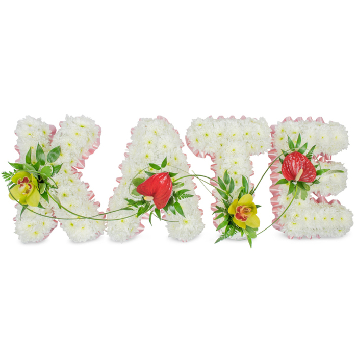 A bespoke name tribute in flowers spells out KATE, the four capital letters arranged side by side against a bright white background that emphasises their clean lines and thoughtful detailing. Each letter is fully padded with compact white chrysanthemums, their petals overlapping to create a dense, cushion-like effect that appears soft to the touch and beautifully uniform. A narrow band of pale pink satin ribbon traces the perimeter of every letter, giving a refined edge and a subtle blush of colour that softens the strong shapes without overwhelming them. Carefully placed amongst the chrysanthemums are elegant accent blooms: on the left of the K and at the foot of the T, lime-green cymbidium orchids with intricate reddish-brown throats introduce a fresh, luminous tone; on the A and E, rich red anthuriums, distinctly heart-shaped and slightly glossy, bring a bold, emotional focal point. Around and beneath these feature flowers, layers of lush green foliage - from glossy leaves to feathery ferns - add contrast, volume, and a natural garden feel. Fine, flexible green tendrils arc gracefully between the letters, visually tying K, A, T and E into a single flowing composition rather than four separate forms. The overall mood is one of calm dignity and tender affection, making this design especially suited for a funeral service or celebration of life in Golders Green, perhaps arranged by Flowers Golders Green for delivery to a local chapel, crematorium, or family home as a truly personal gesture of sympathy and remembrance.