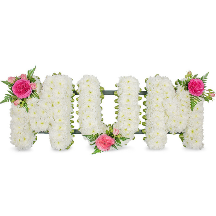 The image presents a serene MUM floral tribute, carefully arranged to capture both clarity and emotion, as if prepared for a service at a chapel or family gathering in Golders Green. Three bold capital letters form the word, each one outlined by a subtle dark green frame that supports a dense blanket of white spray chrysanthemums. The chrysanthemums completely fill the shape of every letter, packed so closely together that they create a plush, even surface, giving the impression of a soft cushion of petals. Their bright yet gentle white tone symbolises purity, remembrance, and a peaceful farewell, making the tribute instantly recognisable from across a funeral chapel or crematorium hall. To soften the structure and personalise the design, three matching accents of pink flowers and foliage are woven into the white base. On the upper left shoulder of the first M sits a focal cluster: a bold fuchsia garden rose fully unfurled, surrounded by smaller, lighter pink spray roses and framed with airy fern fronds. At the base of the central U, another cluster nestles into the lower curve, with the same vibrant rose tones and light green ferns stretching outward. The second M is balanced with a final cluster on its upper right shoulder, mirroring the first and completing a gentle diagonal flow of colour from left to right. The fern foliage adds movement and a woodland freshness, echoing the greenery so familiar around Golders Green. Set against a clean white backdrop, the tribute feels calm, dignified, and deeply personal, a fitting floral expression of love, thanks, and remembrance for a much-loved mother.