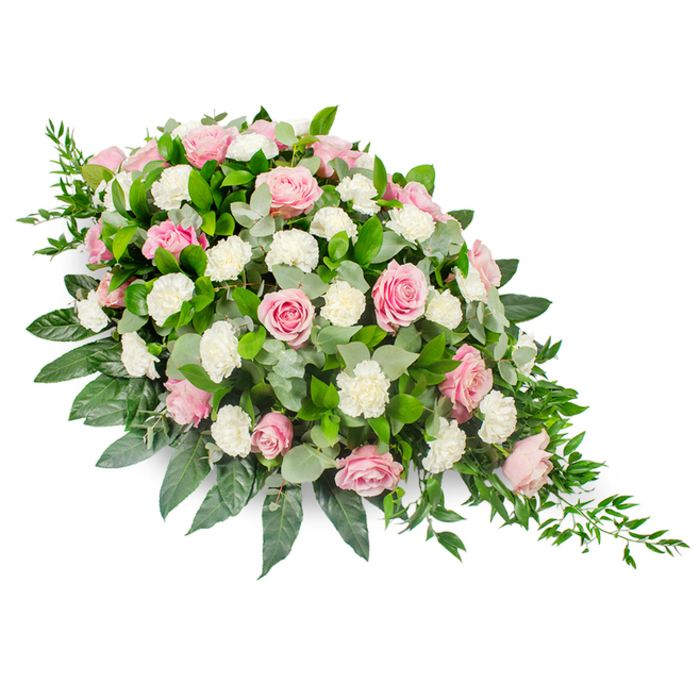 A large, elegantly composed funeral spray is captured against a crisp white background, shaped into a graceful teardrop that swells generously at the head and narrows to a gentle, tapered point. The dominant elements are soft pink roses and snowy white carnations, interwoven to create a harmonious, flowing design. The roses, some still partially closed with protective outer petals, and others fully open in broad, layered spirals, show a range of pinks-from pale, almost milky blush through to deeper, more romantic rose tones. They are arranged in such a way that the eye naturally travels along the length of the spray, following the subtle shifts in colour and petal shapes. Between these roses, clusters of white carnations and spray carnations are nestled, each bloom brimming with fine ruffles that catch the light and lend a gentle, cloud-like softness. The flowers are supported by a substantial base of foliage: dark green, glossy leaves that trace the edges, providing a strong silhouette, and round eucalyptus leaves in a cool, silvery green that peek through the blooms, adding depth and an understated hint of movement. At the narrower end of the spray, delicate strands of trailing greenery extend outward in a soft cascade, giving the arrangement a sense of continuation beyond its physical boundaries. This thoughtful interplay of form and texture gives the tribute a feeling of quiet luxury and sincere affection. It is the sort of arrangement a family in Golders Green might select to accompany a loved one on their final journey, reflecting both the calm dignity of local services and the tender memories held by those gathered to say goodbye.
