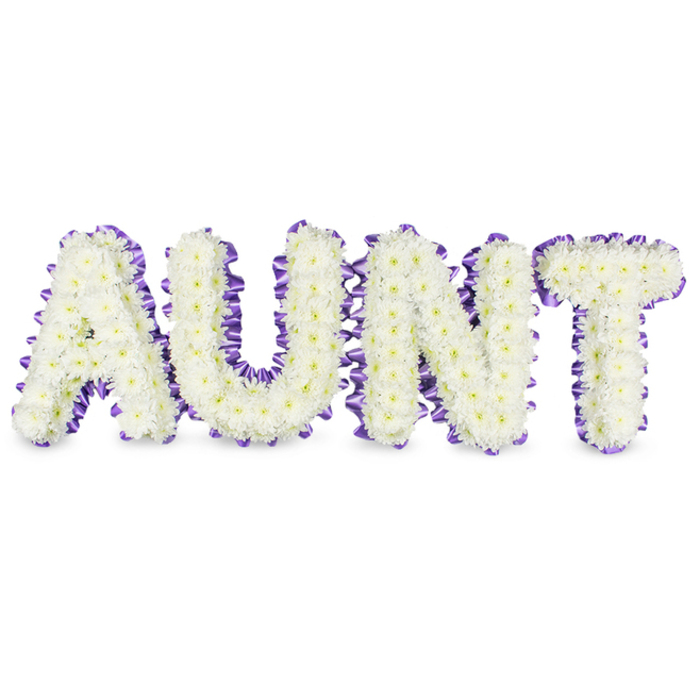 A handcrafted floral letter tribute spells out 'AUNT' in large, graceful capitals, each letter densely packed with immaculate white spray chrysanthemums whose tiny, layered petals create a soft, tactile surface like fresh winter clouds. Here and there, pale yellow centres show through the massed white florets, offering delicate points of warmth that catch the eye and alleviate the pure palette. The edge of each letter is defined with a sumptuous purple satin ribbon, gently ruffled and scalloped to hug the frame and provide a refined, dimensional border that contrasts with the blooms' softness. Subtle grey shadows beneath the letters indicate their three-dimensional construction and separation from the pristine white backdrop, suggesting a real object placed on a chapel floor or beside a family altar. There is an implied freshness to the composition-the cool, green-tinged scent of chrysanthemums and the tactile contrast between the smooth ribbon and the feathery petals. Intended as a personal memorial or sympathy piece, this arrangement carries a tone of loving respect and tender memory, fitting for services or gatherings in Golders Green, whether near the quieter streets off Finchley Road or by the familiar community spaces around Hendon Way. The overall effect is dignified and comforting: a visible, composed expression of love and farewell.