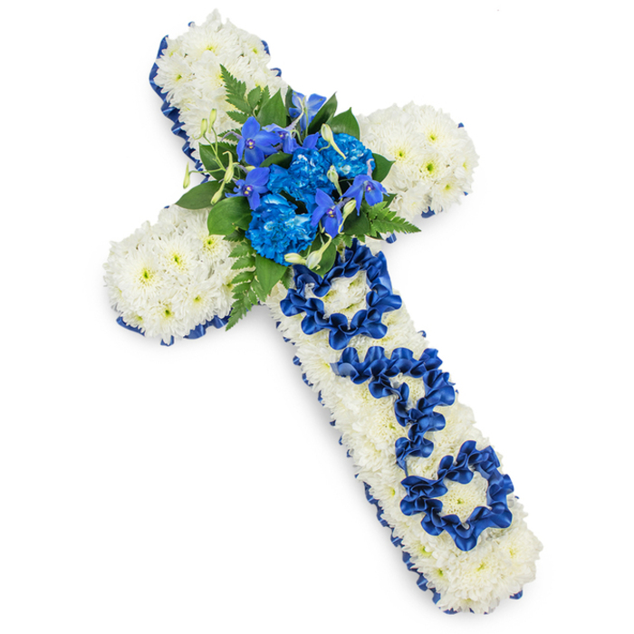 The photograph captures a substantial funeral flower cross, presented flat against a luminous white background so that every nuance of texture and colour is easily imagined. The cross itself is constructed from a dense blanket of fresh white spray chrysanthemums, their small, round blooms placed closely together so there are no visible gaps, giving the impression of an unbroken field of soft white petals. Encircling this foundation is a neatly pleated border of royal blue satin ribbon, its gentle sheen catching the light and creating a striking edge that crisply defines the outline of the cross against the backdrop. At the meeting point of the two arms, a lush spray of royal blue flowers forms the visual centrepiece: full, ruffled blue carnations nestle beside slimmer, vertical blooms reminiscent of blue delphiniums or orchids, their cooler tones and layered petals providing depth and movement. Threaded between the blue blooms are dark green fern fronds and various leafy stems, their feathery and smooth surfaces adding natural contrast and a more organic feel. Along the upright stem of the cross, the word DAD is spelled out not with printed letters, but with loops, twists, and folds of the same royal blue ribbon used for the border, each letter carefully shaped and anchored into the chrysanthemum base. This handcrafted lettering makes the tribute intimate and specific, expressing love and gratitude for a father. The lighting is soft and even, casting a very subtle shadow that hints at the arrangement's thickness and weight. It is a classic, respectful sympathy design, the sort of meaningful floral cross families in Golders Green might send to a funeral at a local church, synagogue memorial, or resting place near Childs Hill or Temple Fortune, to mark a life remembered with quiet pride.