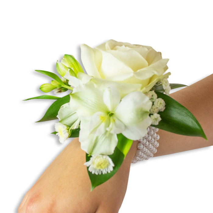 Displayed against a pure white backdrop, this wrist corsage rests on a fair-skinned wrist angled slightly upward from the lower right into the centre, offering a close study in soft whites and rich greens. The focal point is a creamy ivory rose, petals unfurling in tender concentric curves that reflect a soft studio light and convey a quiet luxury. Beneath and to the left, a larger trumpet-style white bloom - reminiscent of alstroemeria or a small lily - presents a pale lime-green throat and gently ribbed petals that add structure and visual depth. Tiny green-tinged buds pepper the arrangement, suggesting movement and future opening, while feathery sprays of baby's breath (gypsophila) weave a translucent veil around the main blossoms. A grouping of small, daisy-like white florets with vivid yellow centres anchors the lower edge of the cluster with a cheerful, contrasting dot of colour.
Several broad, glossy dark-green leaves with a slightly waxy texture frame and support the flowers, their surfaces catching light and enhancing the white blooms' purity. The corsage is secured to the wrist by a refined multi-strand bracelet of round, luminous white pearls that encircle the arm with gentle elasticity, providing both stability and an elegant companion to the flowers. This combination of textures - satiny rose petals, crisp green leaves, airy filler, and smooth pearls - creates a tactile harmony ideal for formal occasions: weddings, proms, or evening receptions in Golders Green, near Golders Hill Park or Temple Fortune. The scent is fresh, faintly floral, and the overall impression is one of handcrafted restraint and heartfelt celebration.