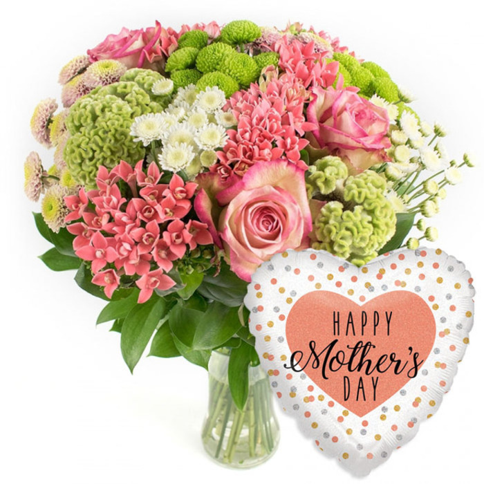 A bright and abundant Mother's Day bouquet with a matching balloon is shown in a studio-style image, set against a spotless white background that highlights every colour and texture. To the left stands a clear glass vase filled with a rounded, carefully crafted arrangement of flowers. Several large pink roses form the romantic focal points; their petals show a soft gradient from deeper pink hearts to paler, almost frosted edges, giving the impression of gentle light falling over them, like the early sun over Golders Green's quiet residential streets. Around these roses gather vibrant coral-pink sprays, similar to kalanchoe or spiky florets, tightly packed to create rich pockets of colour and structure. Lime-green button chrysanthemums and other chartreuse, slightly frilly blooms add a refreshing, modern note, their almost mossy texture offering a tactile contrast you can almost feel beneath your fingertips. Scattered among them, small white daisy-like chrysanthemums bring clarity and brightness, echoing tiny bursts of light. The whole arrangement is embraced by glossy dark green foliage, which curves around the base and between the stems, adding depth and a natural, garden-fresh feel. Through the transparent vase, the straight stems are clearly visible in clean water, suggesting that this bouquet is freshly prepared and ready for local delivery across Golders Green and nearby Hampstead Garden Suburb. On the lower right of the composition, a festive heart-shaped foil balloon leans playfully towards the flowers. Its white or pale silver background is sprinkled with irregular polka dots in shining gold, silver and warm peach tones. At its centre, a solid peach-coral heart contains the words HAPPY Mother's DAY in elegant black type, mixing bold lettering with flowing script. Together, the bouquet and balloon create a complete Mother's Day gift, radiating gratitude, celebration and the simple joy of being thought of by family close to home in NW11.