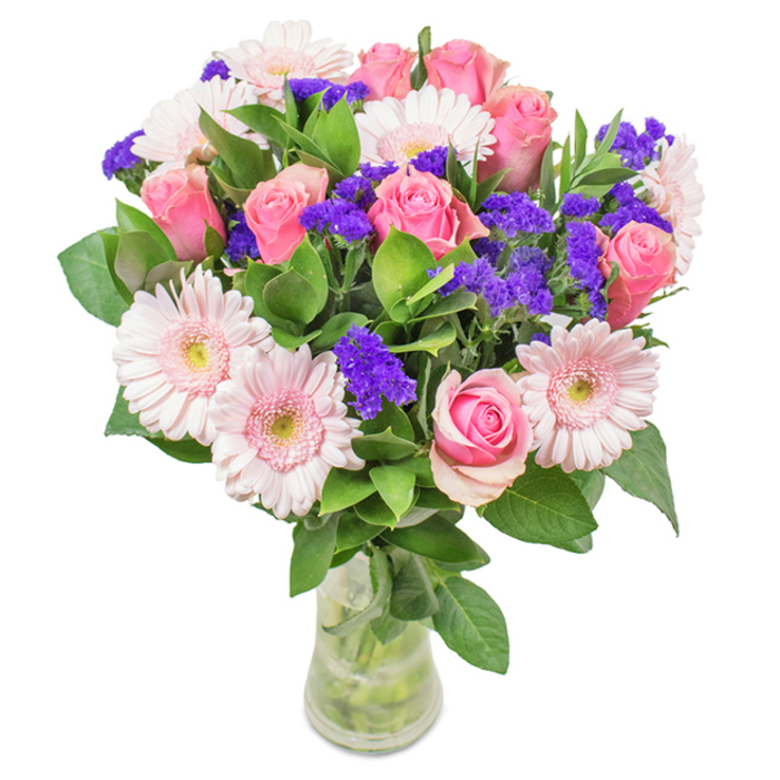 Presented in a crystal-clear glass vase and set against a classic white backdrop, this elegant floral bouquet is the epitome of Golders Green refinement. Around eight perfectly balanced pink roses serve as the arrangement's heart-some tightly furled, others just beginning to bloom, each displaying the iconic spiral formation beloved by local romantics. Interwoven are five to seven pale pink gerbera daisies, each with broad, round faces and subtle creamy centres that allow their soft colouration to shine. Clusters of vivid purple statice act as vibrant accents, their texture and striking tone adding depth and vibrancy that call to mind the lively colours of community gardens near Childs Hill. Anchored by deep green foliage, which provides both structure and a sense of verdant abundance, the bouquet exudes freshness, further enhanced by the visible water and stems within the vase. This arrangement suggests not just expert selection but an appreciation of seasons and celebrations in Golders Green-perfect for birthdays, anniversaries, or welcoming new neighbours. Whether marking a special day or adding a touch of luxury to a residential flat along Finchley Road, this bouquet effortlessly expresses joy, affection, and a deep connection to the area's spirit.