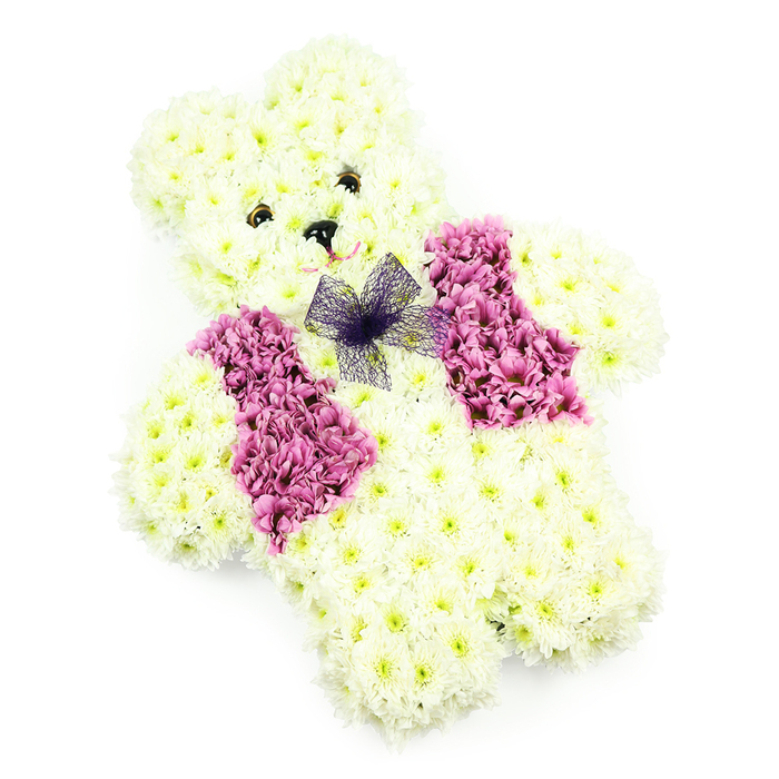 This image shows a teddy bear-shaped floral tribute, carefully arranged so that every petal contributes to a sense of comfort and innocence. Set against a simple white background, the bear appears almost to glow, its form clearly defined yet invitingly soft. The entire silhouette-from the rounded head and perky ears to the compact arms and solid little feet-is constructed from creamy white chrysanthemums. These blooms are closely packed, their feathery petals overlapping to create the illusion of a plush toy's fur, with just enough variation in shade to give natural depth and dimension. The face is expressive without being overstated: two small, dark, bead-like eyes offer a calm, steady gaze, and a tiny black nose is placed neatly in the centre, with a gentle pink curve below suggesting a tender, reassuring smile. Across the teddy's chest, the florist has shaped a neat waistcoat effect using deeper pink and mauve-toned flowers, their richer colour standing out beautifully against the pale body. A delicate bow of violet netting is anchored at the neckline, its translucent loops adding a hint of playfulness and refinement. The lighting is soft and even, with no harsh shadows, so the focus remains on the textures of the petals and the harmony of the colour palette. In Golders Green, where families gather near the crematorium, local synagogues, and quiet residential streets, this type of floral teddy is often chosen for children's funerals, baby farewells, or particularly tender memorials. It serves as a gentle symbol of protection, love, and remembrance, offering a visually soothing presence at moments of deep emotion.