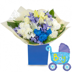 A tender, celebratory bouquet arranged to announce a baby boy, presented with a playful carriage-shaped balloon that reads "It's a Boy." The flowers are gathered into a compact, rounded design and placed in a solid royal-blue gift box that gives the composition a modern, grounded silhouette. Creamy white roses and long, elegant white lilies-some with buds still closed-provide a serene, fragrant core, while plush white spray chrysanthemums add a soft, textural backdrop. Vivid electric-blue chrysanthemums and a striking cluster of deep blue blooms create a vibrant counterpoint, their saturated petals bringing joyful energy. Interspersed among them are clusters of soft lavender or periwinkle blossoms, similar to small hyacinths, which add a powdery perfume and fine detail. Lush greenery, from broad glossy leaves to delicate fern-like fronds, nestles between stems and lifts the arrangement visually from the cream-coloured tissue wrapping gathered neatly at the base. To the right, a pale-blue foil pram balloon floats with darker-blue trim, dotted wheels and tiny heart motifs; the cheerful yellow-green lettering spells out the announcement. The light is soft and natural, catching the shimmer of the balloon and the dewy surface of petals, so the whole set feels intimate and celebratory. Prepared with the care of a Golders Green florist, this bouquet and balloon pair is ideal for hospital doorsteps, baby showers near Hampstead Garden Suburb, or a warm welcome home delivery across the local streets.