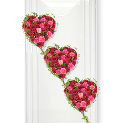 In this image, three opulent heart-shaped funeral tributes drift gently downwards in a graceful diagonal line, each heart meticulously composed from a close-packed carpet of red and pink roses entwined with fresh ivy. The hearts are stacked vertically, like stepping stones of remembrance, beginning at the upper left and moving down to the lower right, giving the entire design a sense of movement and continuity. Each heart is richly textured, created from a mix of tight rosebuds and fully open blooms in deep crimson, vibrant cerise, and soft blush pink, so that the colours seem to ripple across the surface. The petals look velvety and full, conjuring the soft, familiar scent of roses that might greet you at Flowers Golders Green after a quiet walk along Finchley Road. Slender ivy vines trace and soften the edges of every heart, their small, dark green leaves adding a touch of woodland calm, and the trailing stems visually link one heart to the next, symbolising unbroken love and shared memories. The clean, white background acts like a still, luminous canvas, reflecting light back onto the flowers so each tone appears fresh and vivid, with only the faintest hint of shadow adding depth. The composition is romantic yet respectful, ideal as a tribute at a funeral or memorial service in or around Golders Green, where families gather to say farewell. It suggests devotion that continues beyond parting, making this design fitting for commemorating a partner, parent, or lifelong friend whose love left a lasting imprint.