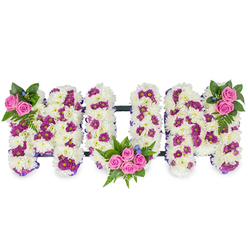 This carefully shaped sympathy tribute spells out MUM in three robust, sculpted letters, presented on a simple white backdrop so the arrangement's textures and colours are front and centre. Each letter's foundation is a thick carpet of snowy white chrysanthemum heads, their tightly layered petals forming a plush, soft surface that catches cool morning light and suggests purity and lasting affection. Scattered through the white are clusters of deep purple-magenta spray flowers, small pom-like blooms that create pockets of colour and a gentle visual cadence across the word. Cheerful yet reverent pink spray roses provide the arrangement's focal accents: a petite cluster of two to three roses rests at the top left of the first M; the U cradles a more generous posy of four to five pink roses within its lower curve; the final M mirrors the first with a matching rose cluster at its top right. Interspersed fern fronds and rich green foliage add shadow and movement around the roses, while tiny blue accent flowers lend a cool highlight that draws the eye. A slim, dark horizontal bar links the letters, lending structural unity without overpowering the floral work. As a local florist in Golders Green, Flowers Golders Green often styles tributes like this for services near Golders Hill Park, Finchley Road chapels and neighbourhood venues, balancing traditional white with softer colour for a comforting, tactile tribute that reads both as mourning and celebration.