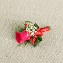A single handcrafted boutonniere rests on a pale beige, woven fabric that looks like fine linen, its subtle texture providing a gentle, neutral stage for the colours of the flowers to glow. In the centre, a luxuriant rose in deep fuchsia pink draws the eye, its petals smooth and velvety, spiralling from a tight heart into looser outer layers that suggest it has just opened to perfection. Around the base of the rose, airy clusters of baby's breath form a halo of tiny white blooms, their softness evoking tenderness and innocence, as if chosen for a heartfelt wedding at a small venue near Golders Green station. Scattered among these delicate flowers, glossy red hypericum berries add a jewel-like brightness, their rounded forms bringing warmth and a festive note, perfect for winter weddings or joyful celebrations. The greenery is thoughtfully arranged: darker green leaves are carefully curled and shaped to give structure, while slender, fern-like fronds stretch outward with a feathery lightness that introduces movement and a touch of wild, garden charm. All the stems are firmly wrapped in a rich red satin ribbon, the fabric smooth and lustrous, folded with care and tied into a compact bow that feels both traditional and stylish. The lighting is soft and even, without glaring highlights, allowing the deep pink, crisp white, shiny red, and layered greens to sit harmoniously together. This meticulous floral accessory, crafted with the kind of attention you'd expect from a trusted Golders Green florist, feels ideal for a groom, groomsman, or formal guest wanting a refined yet expressive touch on their lapel.