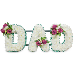 This photograph presents a respectfully crafted funeral lettering piece that reads DAD in large, sculpted capitals, each formed from a thick mass of pure white chrysanthemums that create a soft, pillowy surface. The letters are crisply defined by a vivid emerald green ribbon with a pleated, ruffled finish that traces both the outer and inner contours, producing a refined contrast between the cool green border and the warm white blooms. A subtle dark green or slate-grey support bar passes behind the letters, hinting at a sturdy, stand-ready design for display at a service or a graveside. Carefully placed floral accents lift the overall composition: the first 'D' bears a cluster on its upper left curve, the 'A' cradles a bouquet in the lower V, and the final 'D' is accented on the upper right curve - each cluster composed of rich magenta roses, small white freesia or spray blossoms, and deep, glossy foliage for depth. The sensory impression is understated - the soft, powdery texture of the chrysanthemums, the discreet perfume of roses, and the green, almost citrusy lift of freesia. A florist familiar with Golders Green and surrounding streets like Finchley Road might arrange this for a service at Golders Green Crematorium or a quiet memorial by local parks; its balance of tradition and personal warmth makes it a dignified expression of love and farewell.