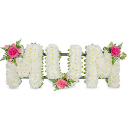 A lovingly crafted MUM tribute stretches horizontally across the image, the three block letters resting on a discreet dark green frame that hints at the sturdy support beneath the blooms, much like the quiet strength of families gathering in Golders Green during times of loss. Each letter is densely covered with small white chrysanthemums, every floret pressed closely to its neighbour so the surface looks like a soft quilt of petals. The white flowers form a smooth, cushion-like texture that suggests peace, purity, and reflection, suitable for display at a funeral service or graveside in one of Golders Green's tranquil cemeteries. Along the upper left edge of the first M, a vibrant cluster of fuchsia and pink roses introduces a touch of warmth: a large, ruffled garden rose in deep fuchsia takes centre stage, surrounded by paler pink spray roses and delicate green ferns. The U holds a similar cluster at its lower central curve, tucked in as if gently cradling a memory, and the second M is crowned on its upper right corner with an almost identical grouping, creating a visual rhythm across the word. The fern foliage fans out lightly from each cluster, its fine serrated leaves adding movement and a natural, garden-fresh feel reminiscent of nearby parks and green spaces. Against the plain white background, the tribute appears almost to float, drawing the eye straight to the loving word MUM. This arrangement quietly conveys respect, tender gratitude, and remembrance, reflecting the sensitive craftsmanship you would expect from an experienced Golders Green florist.