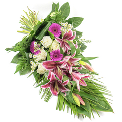 Set against a clean white background, this elegant sympathy spray appears as though it has just been arranged on a workbench in a quiet Golders Green flower shop, ready to be delivered to a nearby chapel or home. The composition stretches diagonally from top left to bottom right, creating a soft crescent or teardrop form that naturally draws the eye along its flowing line. At its heart, dramatic Stargazer lilies unfold in rich fuchsia-pink, their petals tipped in white and scattered with deep burgundy speckles, some blooms fully open and others still held in green-tinted buds. Around these striking lilies, plush magenta gerbera daisies add a lively note of colour, symbolising treasured memories, while creamy white roses and gently ruffled white carnations introduce a calm, serene contrast that speaks of respect and peace. Tiny clusters of white daisy-like filler flowers weave between the larger blooms, adding delicate texture and a sense of softness. The flowers are embraced by abundant foliage: broad, dark green leaves give structure and strength, feathery ferns soften the edges, and long, ribbon-like blades of greenery cascade gracefully towards the lower right, reinforcing the cascading shape. Every element is clearly lit, allowing the vivid pinks, clean whites, and rich greens to stand out without distraction. The overall feeling is one of solemn beauty and quiet hope, well-suited for funerals, memorials, or condolence tributes across Golders Green, Temple Fortune, and the wider NW11 community, when words alone are not enough.