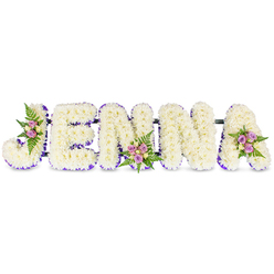 There is a calm artistry to this funeral tribute: the five capital letters of JENNA are formed in three dimensions, each face swathed in tiny, creamy-white chrysanthemums that create a pillowy, reverent texture against the pure white background. A delicate border of rich purple ribbon traces the inner edges of every letter, giving definition and a dignified touch of colour that complements the softness of the white blooms. Thoughtful accent clusters appear on three letters - the upper curve of the J, the lower centre of the second N, and the upper right sweep of the A - where pale pink and soft lavender spray roses mingle with touches of cream roses and feathery dark green fern. Those small groupings bring gentle colour and a whisper of scent to an otherwise serene surface, like handwritten remembrances tucked into the floral lettering. Subtle dark connecting bars hold the letters securely together, suggesting both structure and continuity; the whole piece reads clearly from a distance yet reveals intimate detail up close. The lighting is gentle, a soft studio glow that highlights petal edges and the velvet of the ribbon without harsh shadows, so the arrangement feels both present and consoling. Designed as a sympathetic tribute for a funeral or memorial, this floral name piece offers a personal, composed way to honour someone at a chapel, crematorium, or family service - a visual expression of respect, love, and enduring remembrance that balances purity with soft colour and thoughtful craftsmanship.