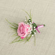 Laid carefully on a pale beige fabric that looks like finely woven linen, this pink rose boutonniere feels like a quiet moment before the celebration begins, perhaps in a home off Golders Green Road as final touches are added to a groom's attire. The single rose is the star, angled slightly to the left, its petals unfolding in a gentle, almost shy spiral. The colour transitions from a rich, confident fuchsia along the outer edges to a softer, powdery pink at the tightly wound centre, suggesting freshness and tenderness. Surrounding the rose, small tufts of white Baby's Breath are tucked between the petals and leaves, like tiny puffs of cloud, each blossom no bigger than a pinhead yet collectively creating a halo of softness. Wisps of slender, grass-like greenery reach outward, giving the design movement and a natural, just-picked charm, as though gathered from gardens around nearby Hampstead Heath. At the base of the flower, a single deep green leaf is curated into a graceful curve, forming a protective cradle, and a few glistening droplets of water cling to its surface, emphasising the flower's vitality. The stems are neatly bound with a smooth satin ribbon in a delicate light pink, wrapped tightly and evenly to create a polished, comfortable grip. At the very end, a deeper magenta-pink ribbon forms a small, tidy bow, adding a note of contrast and sophistication. The muted, textured background ensures that every detail of the boutonniere's craftsmanship is visible, making it an ideal finishing touch for weddings, civil ceremonies, or black-tie events across Golders Green and the surrounding North West London neighbourhoods.