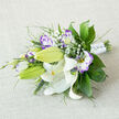 Resting on a neutral, light beige linen, this horizontally arranged bouquet reads like a crafted moment captured by an experienced local florist: large, pristine white Oriental lilies form the central focus, their satin-smooth petals arching back to expose golden-orange stamens speckled with dark pollen and delicate reddish-brown markings that add quiet character. Several lilies hold as tight green buds, a visual promise of unfolding life. Interspersed among them, white and purple lisianthus (eustoma) offer ruffled textures-petals soft and layered, fading from a creamy centre to a lively lilac or deep violet fringe that frames each bloom. Small, cloud-like bunches of Baby's Breath thread through the arrangement, introducing lightness and playful negative space between the dominant flowers.
The supporting foliage is rich and varied: broad, deep-green leaves likely ruscus or salal provide a glossy backdrop, while feathery fronds and slender spike grasses add contrast and movement. The stems are bound in a neat white satin wrap, secured with tiny, gem-like pins that catch the light and lend an understated celebratory detail. The composition is slightly asymmetrical but balanced, conveying natural grace rather than strict formality.
As a Golders Green florist product, this bouquet-available for local delivery across Golders Green and nearby Finchley Road-carries a soft fragrance where the lilies' gentle spice meets the sweet notes of eustoma. Photographed in soft morning light, it feels ideal for a wedding bouquet, an intimate anniversary, or as a tasteful gift for family and friends in the neighbourhood, reflecting the refined, seasonal sensibility of Flowers Golders Green.