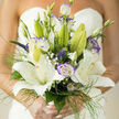 Crafted for a bride who loves quiet refinement, this hand-tied bouquet centers on large, pristine white lilies whose open faces catch a soft London morning light. Each lily's silky petal unfolds with the kind of smooth, tactile luxury that invites a gentle touch; scattered among them, lisianthus blooms edged in a subtle purple introduce romantic contrast and a watercolor-like softness. Fine, airy grasses and delicate green filigree frame the composition, their featherlight motion creating gentle flow around the central blooms, while tiny gypsophila clusters add a lace-like innocence that punctuates shadowed corners. Slender veronica spikes and a few still-closed buds give vertical interest and a sense of promise, echoing the upward reach of the lilies themselves. The perfume is tender-lily sweetness tempered by fresh, leafy undertones-filling close spaces with a memory of spring. Sunlight brushes the bouquet so the whites glow warm and the violets read cool, creating a harmonious tonal balance that feels serene and celebratory at once. As a florist operating near Golders Green tube and Golders Hill Park, I arrange each stem so the bouquet sits light and confident in the hand; at Flowers Golders Green we focus on bouquets that carry emotion as much as beauty, available for thoughtful local delivery when a personal touch matters. The overall impression is one of classic elegance with a contemporary whisper, perfect for ceremonies where every detail is chosen with care.
