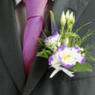 Pinned above the heart on a dark, well-cut jacket, this boutonnière combines classic refinement with a crisp, contemporary twist-a small composition that speaks louder than its size. The central white lisianthus, edged in a striking violet-purple, opens like a quietly radiant star, its velvety layers catching soft light. Complementing it is a compact dianthus with white petals ruffled in lively purple, introducing a playful textural contrast. Wisps of gypsophila lace the arrangement with airy white points, while slim ornamental grasses and deep green foliage arch and cradle the blooms, suggesting movement and new growth. A single spike of deep indigo veronica adds elegant height and an unexpected vertical line, balancing the rounded forms below. Everything is gathered with a crisp white ribbon whose clean fold speaks of careful hands and considered design-details our workshop at Flowers Golders Green attends to daily when preparing pieces for ceremonies along Finchley Road, Hoop Lane and around Golders Hill Park.
Beside a lustrous magenta tie, the boutonnière reads as thoughtful and slightly bold; the materials hold a soft, garden-fresh scent and a subtle tactile richness that invites a gentle touch. It's well suited to weddings, anniversaries and commemorative gatherings in the local community, where small botanical accents carry personal meaning. The overall effect is one of sophistication without fuss-a wearable keepsake that holds tenderness, anticipation and the quiet expertise of a neighbourhood florist.
