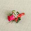 In this refined boutonnière, the drama centers on a fierce magenta rose, its petals soft and velvety, coaxed just enough to reveal the bloom's elegant spiral. Clusters of tiny white gypsophila surround the rose like miniature stars, adding an airy purity that softens the composition. Plump red hypericum berries nestle among the stems, their smooth, cherry-like sheen echoing the rose's warmth and providing a joyful, almost celebratory accent. Delicate, grass-like sprigs-suggestive of asparagus fern-sweep outward with a natural, botanical motion, while broader, folded aspidistra leaves form a deep-green architectural backdrop, giving structure and a sculptural edge. The whole assembly is bound with a rich crimson satin ribbon, wound tightly and tied into a small, elegant bow; the ribbon's cool silkiness contrasts pleasingly with the rose's velvety texture and the berries' gloss. Laid diagonally across a pale beige linen backdrop, the arrangement's colours read vividly against the neutral weave, the soft lighting emphasizing petal contours and leaf folds. The scent is a gentle whisper of rose and green stem-a memory-maker for weddings, proms, or anniversaries-crafted with the patient attention of a neighbourhood florist. Made with fresh, locally sourced stems and designed to sit comfortably on a lapel, this boutonnière reflects the quiet sophistication we bring to orders around Golders Green Station and the surrounding streets; Flowers Golders Green can prepare similar pieces for same-day or scheduled delivery in the area, ensuring each detail arrives fresh and firmly in place.