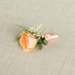 In gentle, natural light a single peach rose is shaped into a boutonniere that radiates understated romance and artisanal care. The flower's petals are layered in warm apricot gradations, the heart holding a richer golden-apricot depth that softens to pale peach at the tips, creating a luminous, velvety surface that seems almost touchable. Delicate sprays of gypsophila punctuate the arrangement like tiny bright stars, bringing a whisper of innocence and airy texture that lifts the composition. Deep green blades of foliage form graceful loops around the bloom, their cool tones and glossy finish providing a refined contrast to the soft peach hues. The stem is expertly bound in matching satin ribbon, tied with a small, neat bow whose subtle sheen gathers the morning light; the wrapping suggests both durability and thoughtful presentation. As a local florist's piece, it carries a scent memory of fresh-cut rose tempered by leafy green notes, conjuring mornings spent sourcing flowers near the Broadway and Finchley Road markets. The boutonniere is designed to complement formalwear with a quiet dignity and to photograph with elegant restraint, perfect for weddings, anniversaries, or milestone evenings in Golders Green and neighbouring Hampstead-an emblem of joy that feels both personal and timeless, prepared with care for a day that will be cherished.
