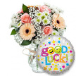A cheery 'Good Luck' gift ensemble captured against a clean white backdrop, arranged with the careful hand of a neighbourhood florist in Golders Green. To the left, a generous bouquet sits in a clear glass vase tied with a simple rustic twine bow; the stems are visible through the glass and the composition feels relaxed yet thoughtfully structured. The flowers are a soft, reassuring palette: powder-pink roses with tightly furled petals, silk-smooth peach gerbera daisies with warm, almost coppery centres, tiny sprays of white baby's breath (Gypsophila) that drift like lace through the blooms, and compact clusters of white and lime-green chrysanthemum florets that give a crisp, lively texture. Deep green foliage peeks between the blooms, lending depth and a cool herbal scent that balances the subtle perfume of the roses. In the foreground, overlapping the base of the vase, a round metallic silver foil balloon gleams with scattered confetti motifs-bright hearts and star shapes in blue, pink, yellow and orange-and carries the bold, playful message Good Luck! in multicoloured, bubbly letters. The two O's in Good are replaced with sunny yellow smiley faces-one winking, the other playfully sticking its tongue out-adding an affectionate, encouraging personality. A small KALEIDOSCOPE logo sits along the bottom rim of the balloon. The overall impression, whether spotted while walking past Golders Green Road or sent for a send-off near Golders Hill Park, is one of warm encouragement: a bouquet that smells faintly of roses and green stems and a balloon that promises bright wishes for exams, interviews, farewells, or any new beginning.