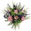 This image shows a lush, rounded bouquet set crisply against a white background, its colours and textures calling to mind a gentle celebration somewhere along Golders Green Road. At its core, clusters of pastel pink and mauve roses unfurl in varied stages of bloom, some delicately cupped, others fully open to reveal layered, velvety petals shaded from deeper rosy centres to soft, almost creamy tips. Interspersed among them, generous carnations in dusty rose and muted mauve create a plush, ruffled texture, giving the arrangement a sense of abundant softness. Piercing through this cushion of petals are tall, slender Veronica spikes in deep violet-blue, adding an elegant vertical rhythm and a hint of contemporary flair. Around these larger flowers, smaller lavender-blue aster-like blossoms and rich purple lisianthus buds and blooms fill the spaces, like constellations scattered across a twilight sky. The foliage provides a refreshing contrast: lime-green, almost chartreuse filler adds sparks of brightness, while cool, silvery eucalyptus and other leaves bring structure and calm, much like the quiet greenery around Golders Hill Park. The stems are neatly bound at the bottom, clearly visible and aligned, showcasing a classic hand-tied finish that suggests expert craftsmanship and readiness for delivery to homes and offices across Golders Green. Though the photo is still, you can almost sense the soft fragrance of roses mingling with the clean scent of foliage, making the bouquet feel perfect for birthdays, anniversaries, or thoughtful get-well wishes, delivered with care in this North West London neighbourhood.