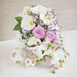 A contemporary yet romantic floral centerpiece rests on a pristine white surface, its colours and textures reminiscent of a calm morning stroll through Golders Green on the way to the park. Dominating the arrangement, several large white Phalaenopsis orchids arch gracefully, their petals smooth and luminous, with golden-yellow and orange centres that draw the eye inward. Tucked among these exotic blooms are fully opened roses in a gentle lavender-pink shade, their tightly layered petals forming soft spirals that speak of devotion and timeless love. Fine sprays of white baby's breath are woven throughout, adding a lace-like veil of tiny blossoms that soften the transitions between the larger flowers. 

Along the edges, slender stems of pale purple lisianthus with richer violet tips offer a delicate ruffle, while cascades of smaller pastel lavender-pink flowers, perhaps stock or sweet peas, spill lightly over the side, suggesting movement and effortless grace. Glossy green leaves, some broad and architectural, others smaller and more delicate, cradle the blooms and provide a fresh, verdant counterpoint to the pastel tones. The flowers rise from an artistic white vase made of interlaced strips, forming an open globe that feels both sculptural and airy, mirrored by two matching woven orbs set to the left at its base. Behind, a softly lit, beige, fabric-textured backdrop creates a warm, diffused glow, allowing every nuance of petal and leaf to stand out. The overall impression is one of refined celebration, ideal for a wedding reception table near Golders Green station, an intimate engagement dinner at home, or any cherished milestone where beauty, calm, and quiet joy are desired.