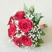 The scene unfolds with a lush, hand-tied bouquet resting serenely on a textured, pale linen cloth, a testament to Golders Green's tradition of elegant celebrations. Rich, velvety red roses-widely open and meticulously selected-take centre stage, their petals spiralling outwards and radiating warmth, depth, and passionate sentiment. Wispy white gypsophila fills the spaces between, introducing a dreamy, cloud-like lightness that softens the arrangement and echoes the early morning fog often found meandering through Golders Green's leafy streets. Sleek, emerald-green foliage provides a crisp, lively contrast, each leaf gleaming with fresh vibrancy as it peeks from behind the blooms. The bouquet's sturdy stems are expertly wrapped in red and white ribbon, a subtle nod to the area's flair for both tradition and festivity, and further adorned with a line of refined pearls, catching the ambient light with a gentle glisten. The composition, gracefully illuminated by diffused natural light, accentuates every velvety petal, frothy white cluster, and the glimmer of pearls, making this bouquet an ideal symbol of love and celebration. Perfect for Golders Green weddings, anniversaries, or heartfelt deliveries across the NW11 community, this arrangement captures the spirit of devotion and elegance that defines local floral artistry.
