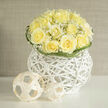 Creamy yellow roses are gathered into a compact, dome-like bouquet, their layered petals opening in gentle spirals that suggest warmth and quiet joy. Fine sprays of baby's breath weave between the blooms, their tiny white blossoms acting like delicate punctuation marks that lift and lighten the composition. The flowers sit within an airy white wicker orb, its architectural curves and tight weave providing a modern base that reads almost like a piece of gallery sculpture. Subtle curling blades of green trace the rim, framing the bouquet and adding a soft graphic edge that complements the roses' roundness.
The scent is evocative: a crisp, sun-warmed aroma reminiscent of fresh-cut fields, with an earthy undernote that grounds the sweetness of the roses-an olfactory memory you might catch while walking from Golders Green station toward Finchley Road on an early summer morning. The lighting captures each nuance of tone, making the pale yellows glow against the clean white of the basket. As a local florist I arrange pieces like this for a range of moments-congratulations, thoughtful remembrances, or understated wedding accents-and I make a point of using fresh stems sourced locally to maintain that field-fresh scent. Available for delivery across Golders Green and nearby streets, this bouquet reflects careful craftsmanship, elegant restraint, and a modern sensibility, the kind of thoughtful arrangement customers ask for at Flowers Golders Green when they want something both beautifully honest and quietly refined.