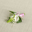 Set against a pale oatmeal-coloured woven fabric, this petite floral boutonniere appears almost like a keepsake moment captured in stillness. The central bloom is a creamy white alstroemeria-style flower, its petals opening softly to reveal delicate reddish-brown stripes along the inner surface, adding a painterly touch that suggests care and craftsmanship. Clusters of tiny white buds, some tightly closed and others just beginning to unfurl, nestle closely around it, evoking the quiet promise of a ceremony about to begin in a Golders Green synagogue or registry office. Wisps of baby's breath drift between the flowers like a fine veil, their many small blossoms forming a gentle halo that lightens the composition. On one side, a bright-green, tapered cone of buds, reminiscent of Ornithogalum, introduces a fresh, textural element-its neat formation almost architectural against the more romantic petals. Surrounding foliage in rich shades of green provides depth and structure: broad leaves create a lush base, while slender, curved blades of grass-like greenery arc outward, echoing the organic flow of stems in a local Golders Green garden after a spring shower. At the bottom, the stems are gathered and wrapped in a glossy pink satin ribbon, tied into a tidy bow that adds a hint of playfulness and celebration without overpowering the gentle palette. The lighting is soft and even, allowing each petal, leaf, and ribbon fold to be clearly defined. The arrangement feels intimate and thoughtful, the kind of floral detail chosen to mark a cherished milestone or to bring a subtle touch of elegance to a suit or dress at a nearby reception venue.