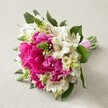 A visually stunning bouquet sits atop a pale, softly textured background, its lush and rounded shape bursting with joyful colour-a true showcase of Golders Green's floral artistry. Large, fully open hot pink peonies dominate, their abundant ruffled petals forming a plush centrepiece that immediately draws the eye. Intertwined among them are crisp white Alstroemeria, their trumpet-like shapes and faint maroon streaks offering delicate detail and light against the vivid pink. Spiky green florets-possibly veronica or hyacinth buds-rise playfully from the arrangement, bringing lively movement and a vibrant springtime feel. Creamy-white, bell-shaped fillers nestle throughout, ensuring the blend remains soft and elegant. Deep green foliage provides a fresh backdrop and accentuates the visual richness, while the entire collection of stems is gathered and secured with a generous flash of bright satin ribbon for a polished, ready-to-carry finish. The bouquet radiates the joy and romance of a Golders Green wedding or special occasion, reflecting the care and expertise found at Flowers Golders Green. Its composition is perfect for a local bride, a centrepiece for a NW11 celebration, or an inspiration for anyone seeking modern elegance rooted in classic beauty.