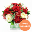 The photograph showcases a richly detailed bouquet that seems to radiate warmth and affection, as if it has just been arranged on a pristine counter in a Golders Green flower studio. Deep red roses, their petals lush and velvety, unfold beside creamy white roses, whose soft, rounded blooms add a gentle lightness and romantic grace. The red and white roses are intricately woven together so that no single flower dominates; instead, they create a harmonious rhythm of colour and texture, evoking both passion and calm. Between these larger blooms, clusters of tiny, vivid red filler flowers, reminiscent of dyed gypsophila, spill lightly through the arrangement, giving a fine, misty quality that softens the transitions and hints at holiday sparkle. Rounded red hypericum berries dot the design like bright beads, offering a tactile contrast and a sense of cheerful abundance that would feel right at home in a cosy flat near Golders Green station. Supporting this tapestry of reds and creams is a bed of fresh green foliage: glossy leaves and sprigs of eucalyptus arc gently outward, introducing notes of blue-green and a suggestion of cool, clean fragrance. All the stems meet in a clear rectangular glass vase, whose straight lines and visible stems give the arrangement a modern, structured character, perfect for a dining table or hallway console in the local area. Around the centre of the vase, a green and white gingham ribbon is wrapped horizontally, bringing a touch of country charm and homely comfort, like a checked tablecloth laid for a family meal. In the bottom right corner of the image, a bright orange circular emblem with white lettering clearly states VASE INCLUDED, making it immediately obvious that the display arrives complete and ready to place. The overall mood is joyful, thoughtful, and quietly luxurious, ideal for gifting on Valentine's Day, anniversaries, or simply to brighten a Golders Green home with fresh flowers delivered the same day.