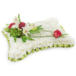A soothing, rectangular floral cushion fashioned entirely from a dense carpet of small white chrysanthemums, presented against a clean white background so every petal reads as a soft, cloud-like surface. The chrysanthemums are packed closely to create a plush texture you can almost feel under your fingertips - cool, slightly satiny, and quietly reflective of light - forming a field of pure white that speaks of peace and repose. A narrow pleated trim of pale lime-green satin ribbon encircles the pillow, its subtle sheen catching the light like a delicate fabric frill and offering a whisper of colour that frames the composition with restrained elegance. At the upper left a considered cluster rises: two open white Oriental lilies with their graceful recurving petals and pale yellow stamens, a closed lily bud for quiet promise, and several deep burgundy spray carnations whose ruffled faces provide rich, velvety contrast against the white. Mixed dark green foliage - feathery fern fronds and broader salal leaves - gives the grouping depth and a natural backdrop, while thin arching strands of bright green bear grass or salal sweep gently across the chrysanthemum plane. Those curves lead the eye to a single, deep red rosebud tucked on the right edge, petals just beginning to unfurl, a poignant symbol of enduring love and remembrance. The overall palette of white, soft lime green, and deep red reads as both solemn and tender, ideal for a funeral or memorial setting. As a local florist arrangement for Golders Green, this pillow-shaped tribute balances traditional sympathy symbolism with careful craftsmanship to comfort grieving families and honour a life with dignity.