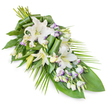 An elegant memorial spray, photographed on a pure white background, showcases a carefully composed blend of white and soft lavender florals arranged in an elongated, diagonal form. The design is fuller at the upper left, where stems and foliage interlace, then gradually narrows towards a subtle point at the lower right, creating a natural sense of movement and calm. At the heart of the tribute are several white oriental lilies, some fully opened with broad, velvety petals and pale stamens, others still in slender buds that rise above the main body of the arrangement, suggesting remembrance and unspoken words. Nestled around them are lisianthus blooms in white, with delicate lavender-tinted edges and fine purple veining that introduces a quiet, restrained colour accent, like the soft hues of a late afternoon sky over Golders Green's residential streets. Clusters of buds add depth and variation, making the piece feel layered and alive. The flowers rest on a substantial cushion of greenery: wide, dark green leaves form a rich base, while certain leaves are folded and rolled into neat, architectural curls near the centre, revealing the florist's skilled touch. From the right side, slim, arching palm-like fronds extend outward, enhancing the teardrop outline and evoking a gentle gesture of release. The overall impression is one of serene dignity and peaceful farewell, a fitting choice for families in and around Golders Green who wish to send a refined floral message of sympathy, comfort, and enduring love at a funeral, memorial, or graveside service.
